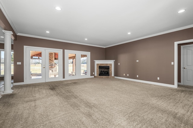 unfurnished living room with crown molding, french doors, a tile fireplace, carpet floors, and decorative columns