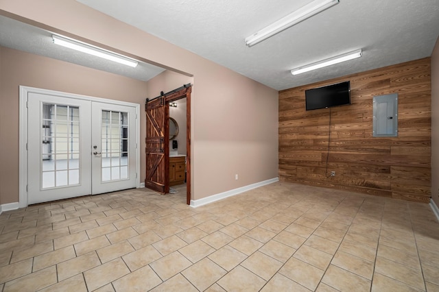 interior space featuring french doors, electric panel, a barn door, a textured ceiling, and wooden walls