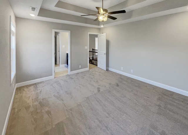 unfurnished bedroom featuring ceiling fan, light carpet, and a tray ceiling