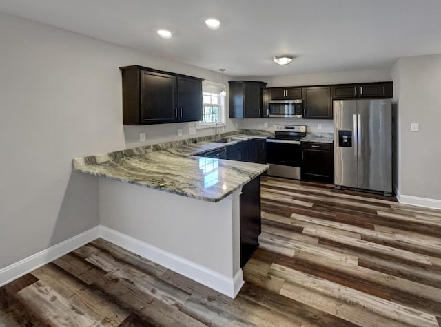 kitchen with kitchen peninsula, hanging light fixtures, appliances with stainless steel finishes, sink, and light stone countertops