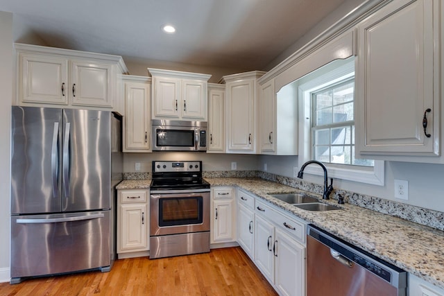 kitchen featuring sink, white cabinets, stainless steel appliances, light stone countertops, and light hardwood / wood-style flooring