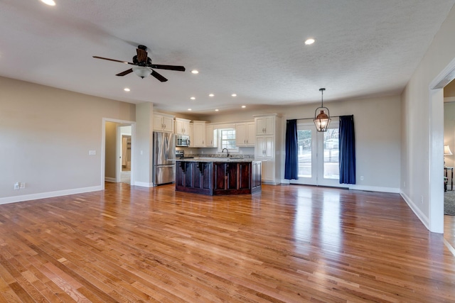 unfurnished living room featuring ceiling fan, sink, light hardwood / wood-style flooring, and a textured ceiling