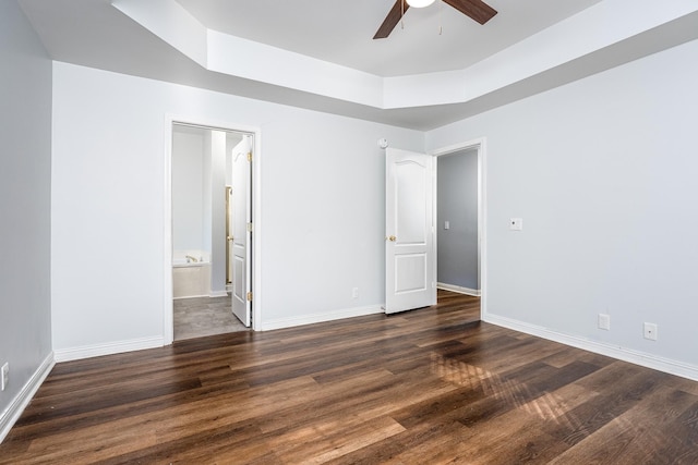 unfurnished bedroom featuring ceiling fan, dark wood-type flooring, ensuite bathroom, and a raised ceiling