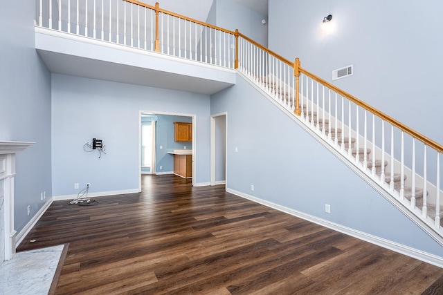 unfurnished living room featuring a high ceiling, dark wood-type flooring, and a high end fireplace