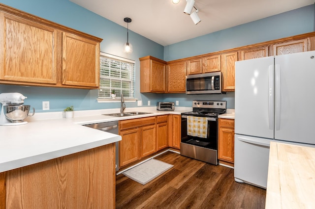 kitchen featuring appliances with stainless steel finishes, dark hardwood / wood-style flooring, sink, hanging light fixtures, and rail lighting