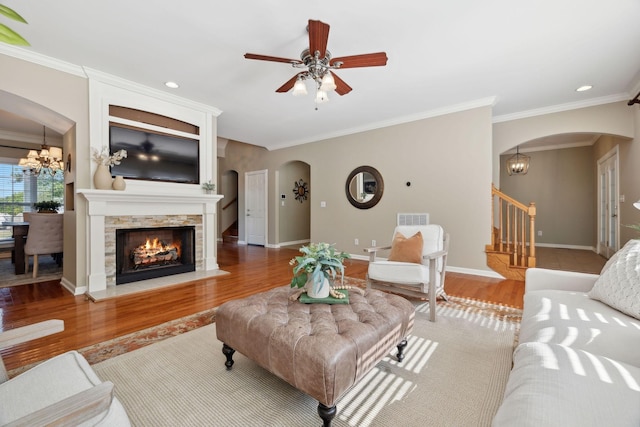 living room with ceiling fan with notable chandelier, crown molding, light hardwood / wood-style floors, and a fireplace