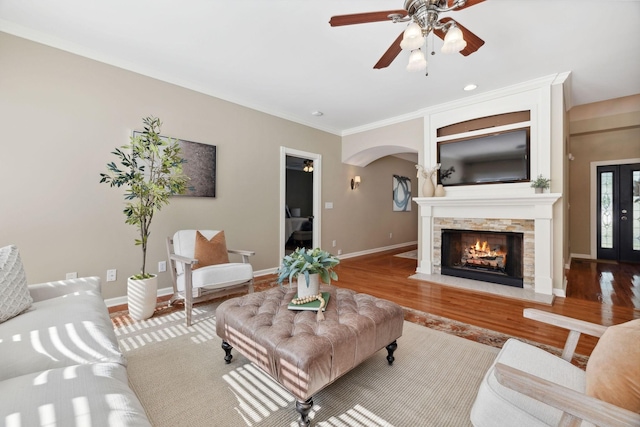 living room with ceiling fan, a stone fireplace, hardwood / wood-style floors, and crown molding