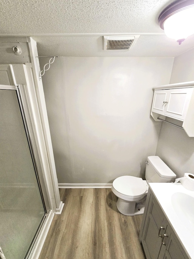 bathroom with hardwood / wood-style floors, an enclosed shower, a textured ceiling, vanity, and toilet