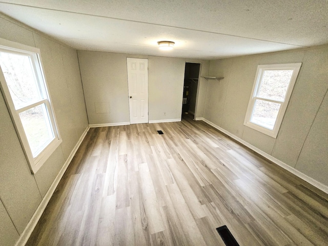 empty room featuring light hardwood / wood-style floors, a textured ceiling, and a healthy amount of sunlight