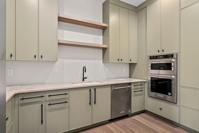 kitchen with sink, light wood-type flooring, light stone countertops, and appliances with stainless steel finishes