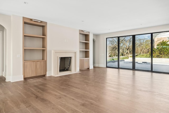 unfurnished living room featuring wood-type flooring, built in shelves, and a high end fireplace