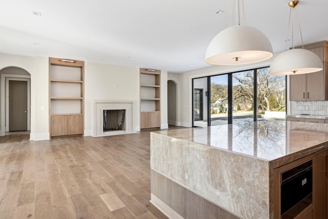 kitchen featuring decorative light fixtures, backsplash, light stone counters, built in shelves, and light hardwood / wood-style floors