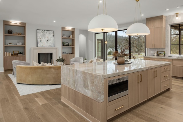 kitchen with light stone counters, a center island, hanging light fixtures, light wood-type flooring, and light brown cabinets