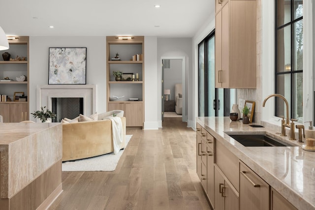 kitchen featuring sink, light hardwood / wood-style floors, light stone countertops, light brown cabinetry, and built in shelves