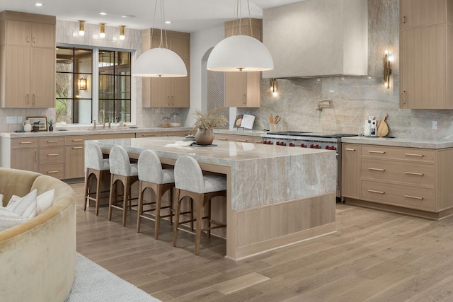 kitchen with light brown cabinetry, a kitchen bar, a center island, high end stainless steel range, and wall chimney exhaust hood