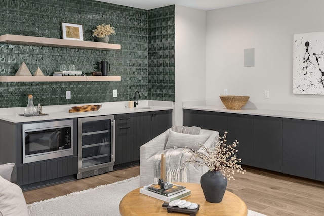 bar with wine cooler, stainless steel microwave, sink, and light wood-type flooring