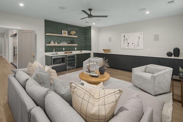 living room with wine cooler, light hardwood / wood-style flooring, ceiling fan, and bar