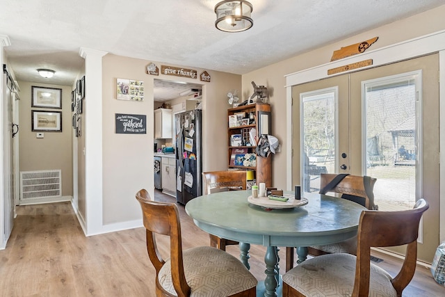 dining area featuring light wood finished floors, visible vents, baseboards, french doors, and a textured ceiling