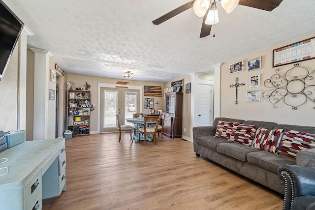 living area featuring baseboards, light wood-style floors, ceiling fan, and a textured ceiling