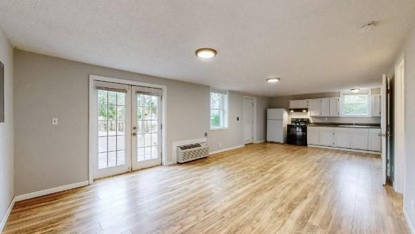 unfurnished living room with light wood-type flooring, a textured ceiling, and french doors