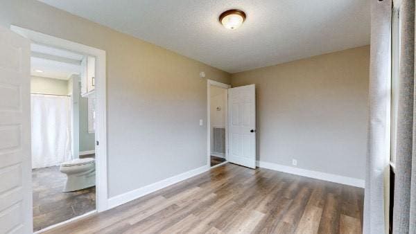 unfurnished bedroom with connected bathroom, hardwood / wood-style floors, and a textured ceiling