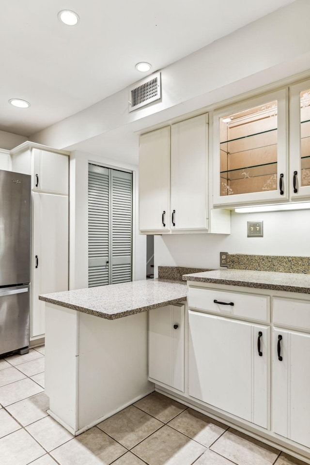 kitchen with white cabinetry, stainless steel refrigerator, light stone countertops, and light tile patterned flooring