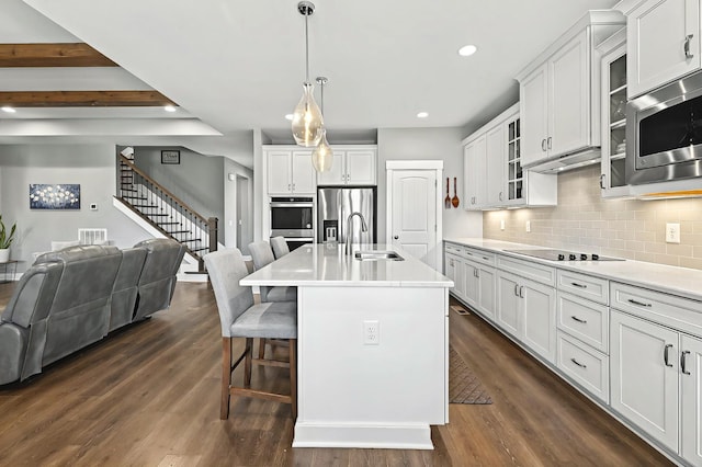 kitchen with white cabinetry, stainless steel appliances, hanging light fixtures, a breakfast bar, and a center island with sink