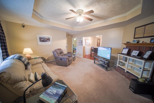 living room with carpet flooring, a textured ceiling, ornamental molding, ceiling fan, and a tray ceiling