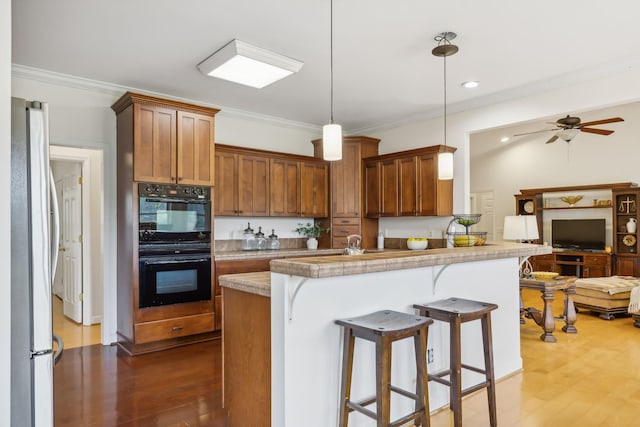 kitchen with pendant lighting, black double oven, dark hardwood / wood-style flooring, stainless steel fridge, and a breakfast bar