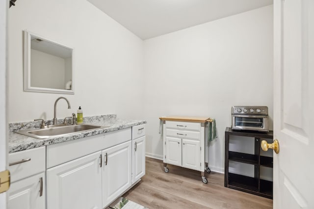 kitchen featuring white cabinets, light stone countertops, light hardwood / wood-style floors, and sink