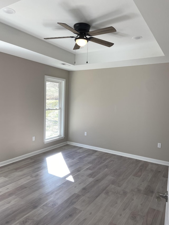 empty room featuring a tray ceiling, dark wood-type flooring, and ceiling fan