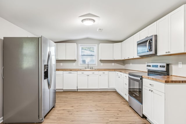 kitchen featuring white cabinets, appliances with stainless steel finishes, sink, vaulted ceiling, and butcher block countertops