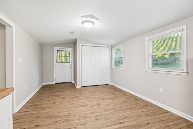 unfurnished bedroom featuring light wood-type flooring, vaulted ceiling, and a closet