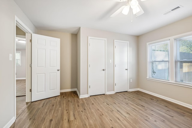 unfurnished bedroom with light wood-type flooring, two closets, and ceiling fan