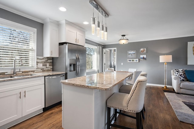 kitchen with white cabinets, a kitchen island, sink, decorative light fixtures, and stainless steel appliances