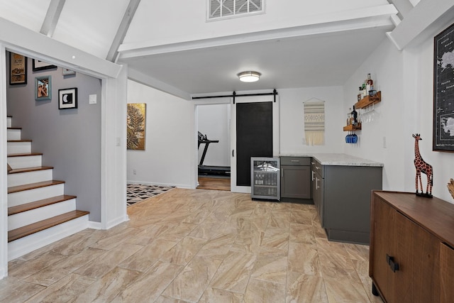 interior space featuring light stone countertops, beverage cooler, gray cabinetry, beam ceiling, and a barn door