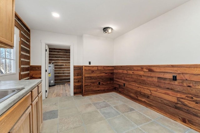 kitchen featuring light brown cabinets, electric water heater, and wood walls