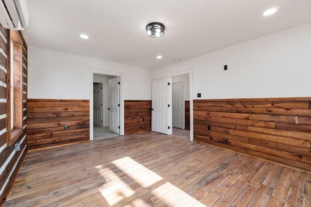 empty room with wood walls, a wall mounted AC, and wood-type flooring