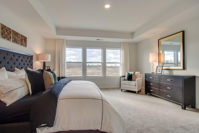 bedroom with light colored carpet and a tray ceiling