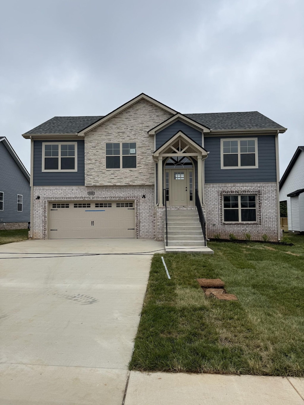 view of front of house featuring an attached garage, brick siding, concrete driveway, a front yard, and a shingled roof