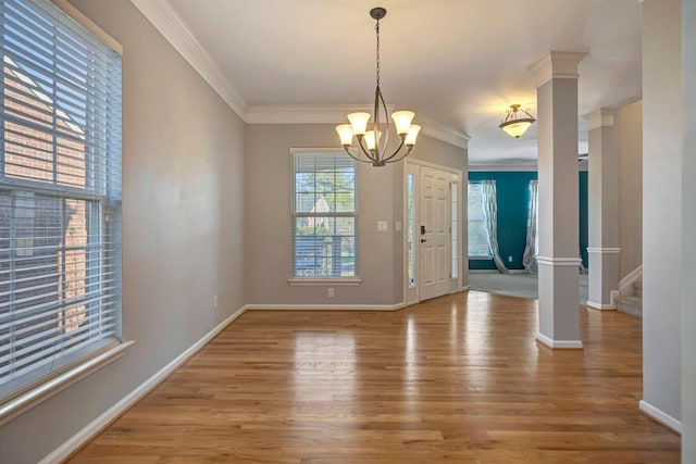 unfurnished dining area featuring hardwood / wood-style floors, crown molding, a chandelier, and ornate columns