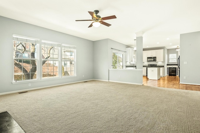 unfurnished living room with beverage cooler, baseboards, visible vents, and light colored carpet