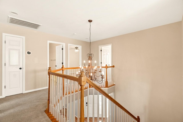 hallway featuring carpet floors, an upstairs landing, baseboards, visible vents, and an inviting chandelier