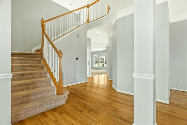 stairs featuring a high ceiling, crown molding, baseboards, and wood finished floors