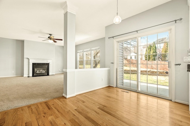 unfurnished living room featuring light colored carpet, a fireplace with flush hearth, a ceiling fan, light wood-style floors, and baseboards