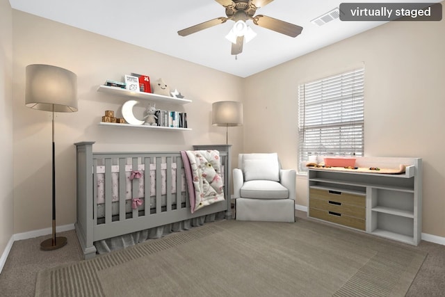 bedroom with light colored carpet, visible vents, ceiling fan, a crib, and baseboards