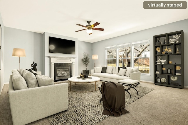 living area featuring a glass covered fireplace, carpet flooring, ceiling fan, and baseboards