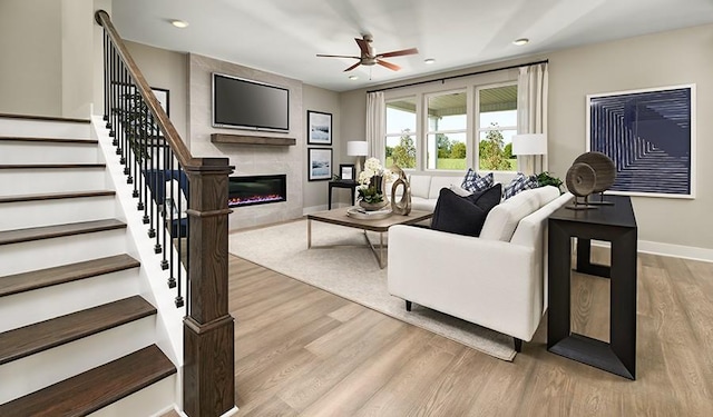 living room featuring ceiling fan, a fireplace, and light hardwood / wood-style floors