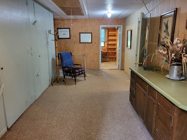 corridor featuring light carpet, a drop ceiling, and wooden walls