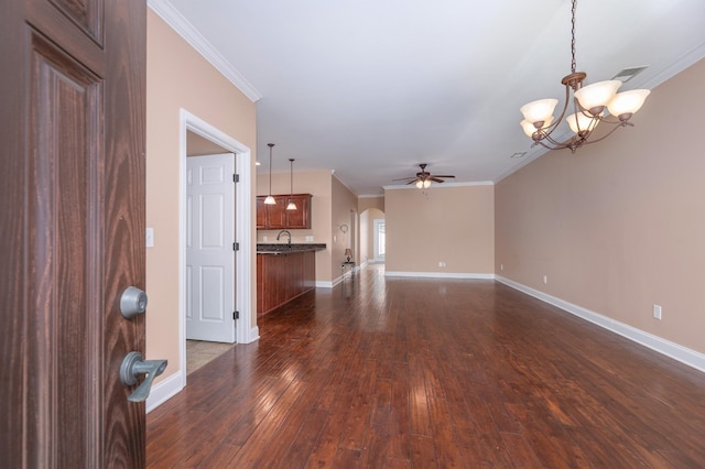 unfurnished living room featuring sink, ceiling fan with notable chandelier, ornamental molding, and dark wood-type flooring